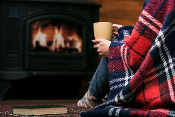Person sitting by fireplace with coffee during winter - home heating season