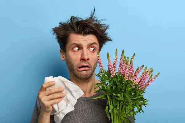 Man suffering from seasonal allergies and pollen holding tissue and flowers - indoor air quality issues Spokane